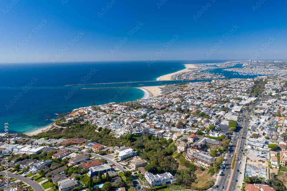 Aerial view over Newport Beach in Orange County, California with coastal neighborhood and homes below on a sunny blue sky day.