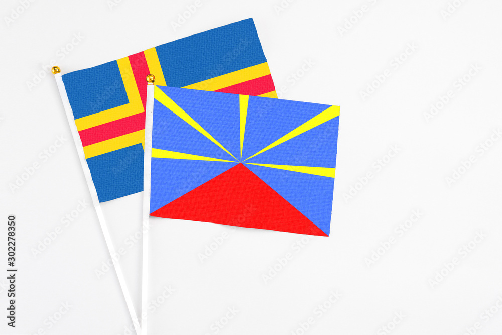Reunion and Aland Islands stick flags on white background. High quality fabric, miniature national flag. Peaceful global concept.White floor for copy space.