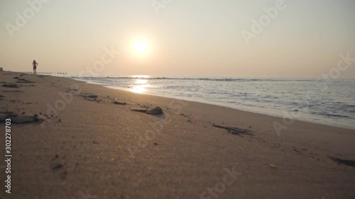 Portrait of unrecognizable woman staying on the sandy beach. Waves of Mediterranean Sea rolling to the sand at sunset or sunrise. Beautiful Turkish nature. photo