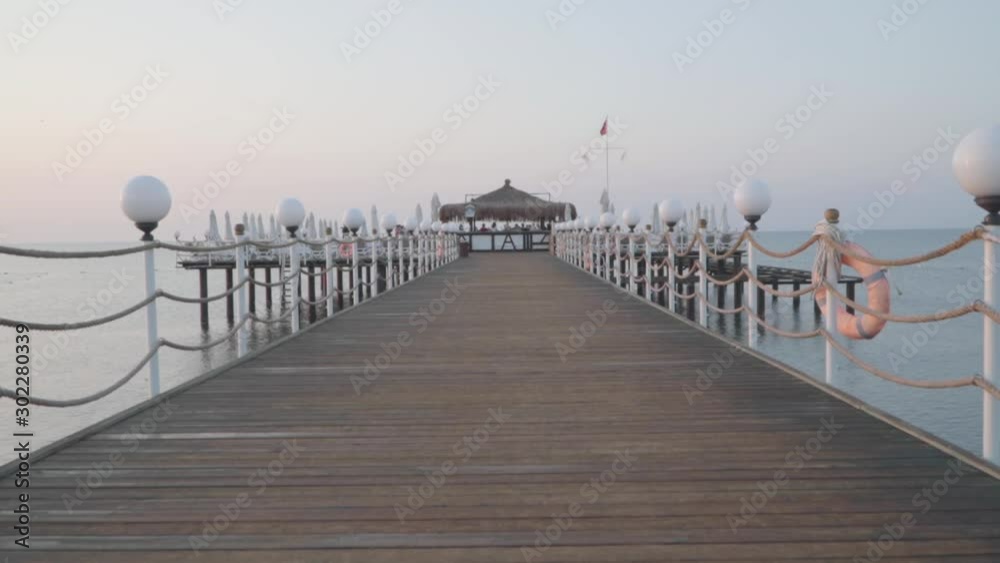 Camera moving forward along the wooden beach ramp. Group of people dancing at the background. Summer day at Eastern resort. Beautiful Turkish nature.