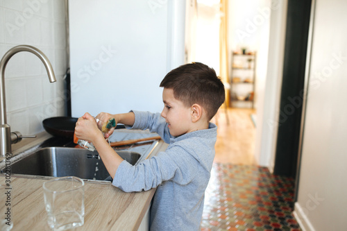 Fotografie Little boy washing dishes and cleaning the kitchen after making dinner