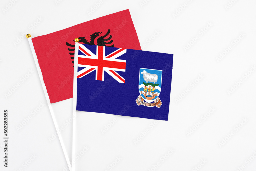 Fototapeta premium Falkland Islands and Albania stick flags on white background. High quality fabric, miniature national flag. Peaceful global concept.White floor for copy space.