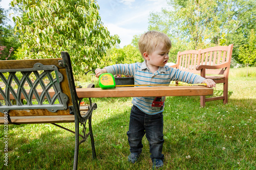 Toddler boy looks serious as he measures a board outside in backyard