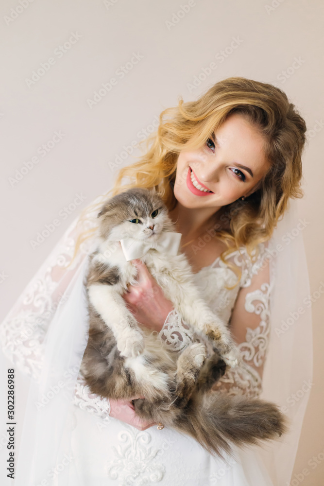 beautiful bride holds fluffy cat with bow tie on wall background