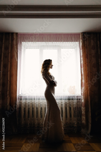 bride in wedding dress crossed arms and looks out the window. pr © Ivan