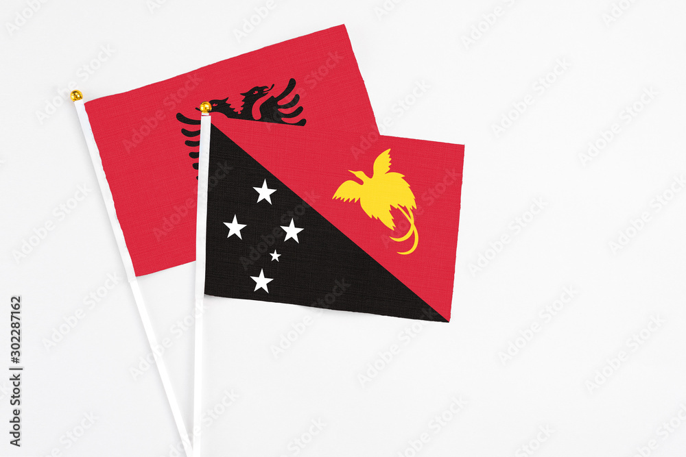 Papua New Guinea and Albania stick flags on white background. High quality fabric, miniature national flag. Peaceful global concept.White floor for copy space.