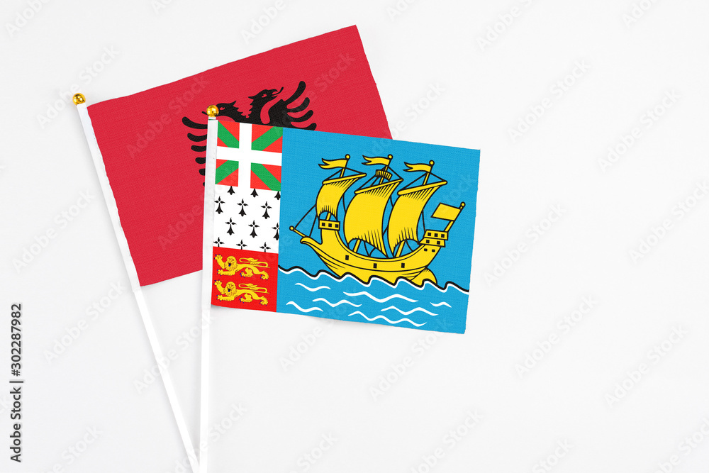 Obraz premium Saint Pierre And Miquelon and Albania stick flags on white background. High quality fabric, miniature national flag. Peaceful global concept.White floor for copy space.