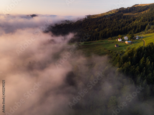 Beautiful morning panorama of forest fnd village covered by low clouds. Summer fog on the mountain hills. Misty woodland.