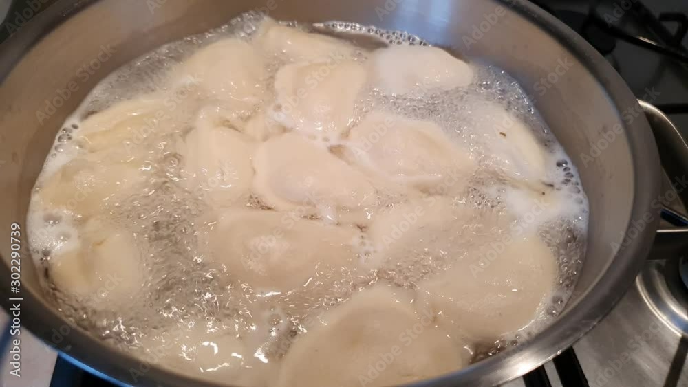 Dumplings with potato are being cooked in boiling water in a steel pan. Vapor is coming out.