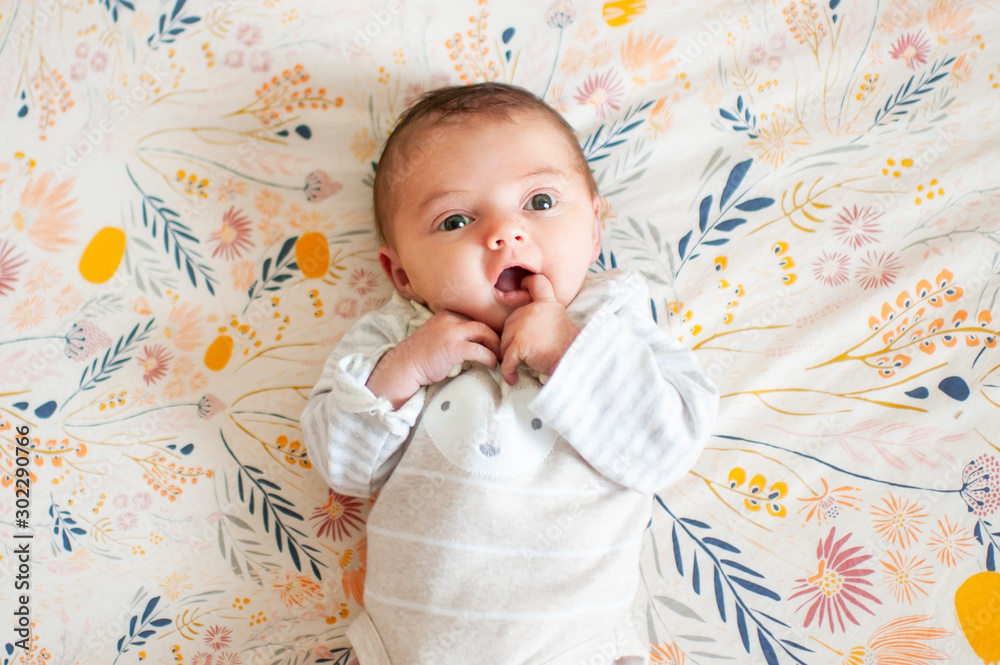 © Cavan Images - Newborn baby girl looking up with cute expression with finger in mouth