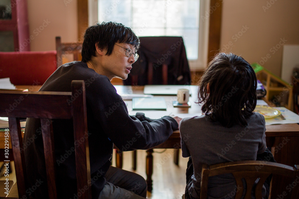 A father tries to help a resistant child with homework at table A father tries to help a resistant child with homework at table