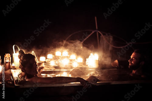 young couple sit in hot tub outdoors at night with romantic candles