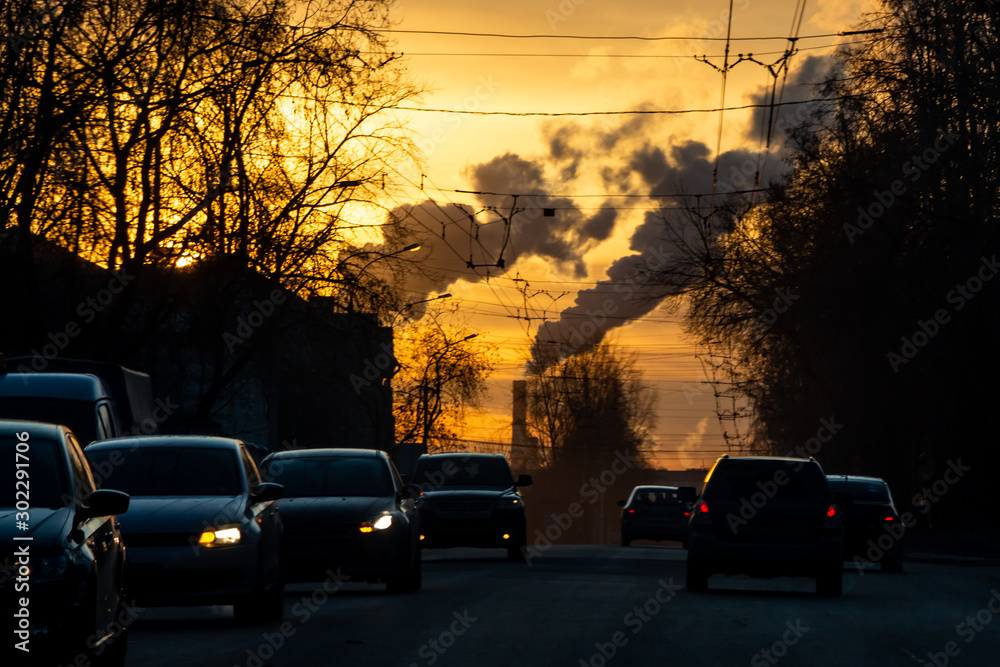 View of the industrial city in in gray and orange smoke with a group of black cars with lights on the road