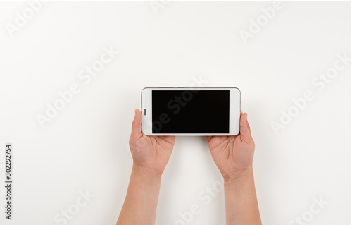 The little girl is holding a horizontally positioned mobile phone. Modern gadgets in the hands of small children. Top view close-up on a smartphone in the hands of a child.