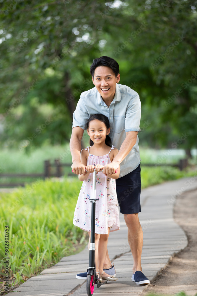 Happy Chinese father and daughter riding push scooter in park Happy Chinese father and daughter riding push scooter in park