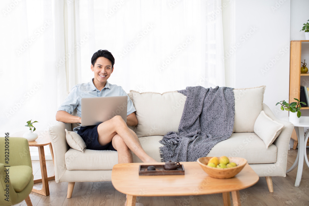 Happy young Chinese man using laptop in living room Happy young Chinese man using laptop in living room