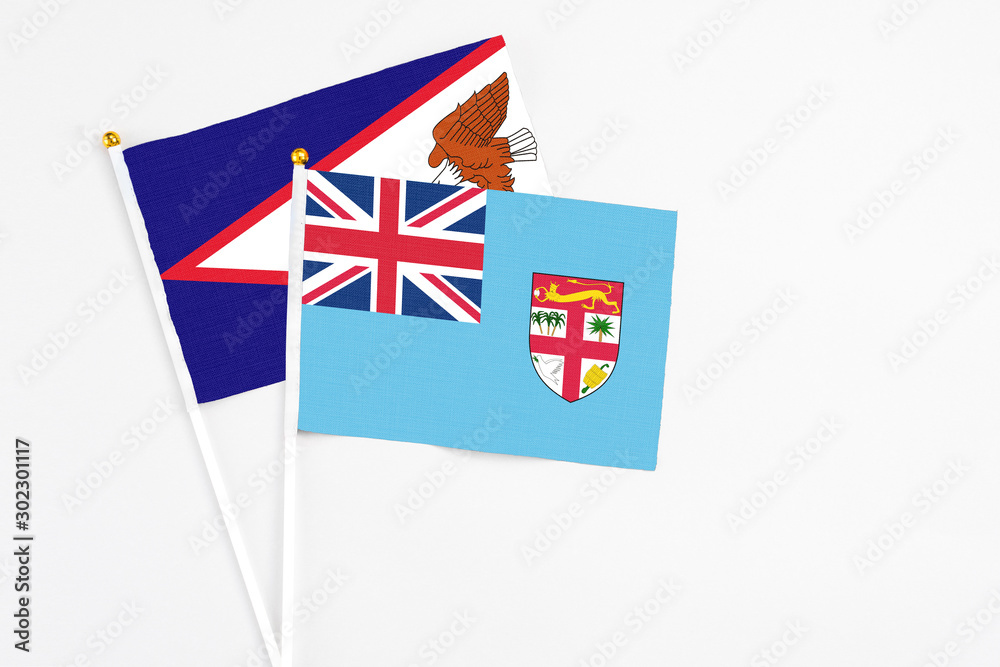 Fototapeta premium Fiji and American Samoa stick flags on white background. High quality fabric, miniature national flag. Peaceful global concept.White floor for copy space.