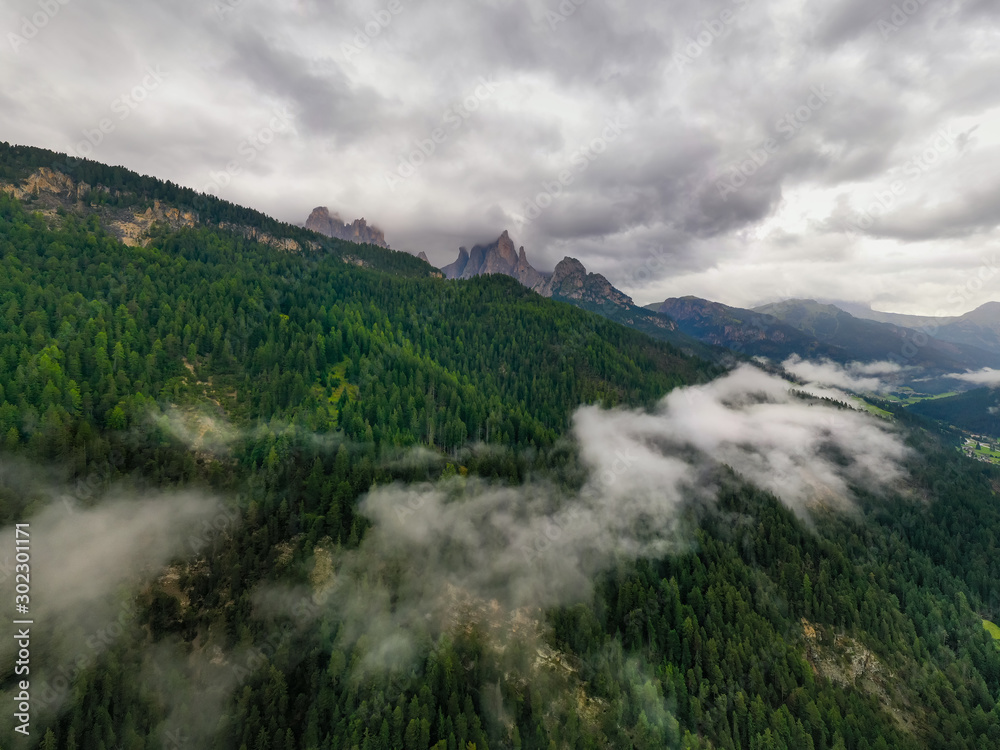 Beautiful aerial panoramic view of the Dolomites Alps, Italy. Mountains covered by clouds and fog. Catinaccio mountain ranges. Fassa Valley, Val di Fassa on the background