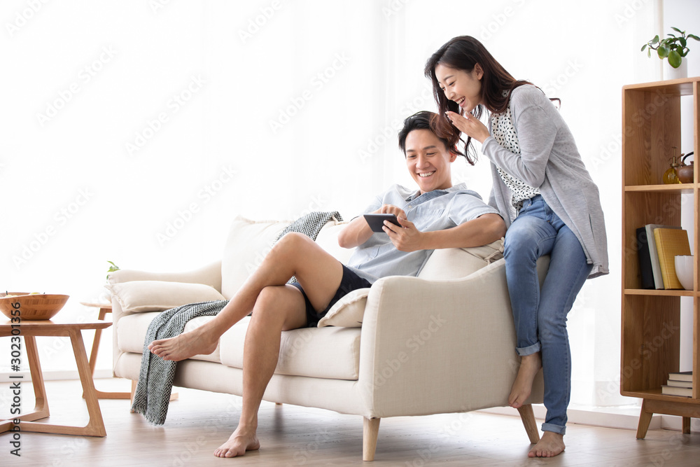 Happy young Chinese couple using smartphone in living room Happy young Chinese couple using smartphone in living room