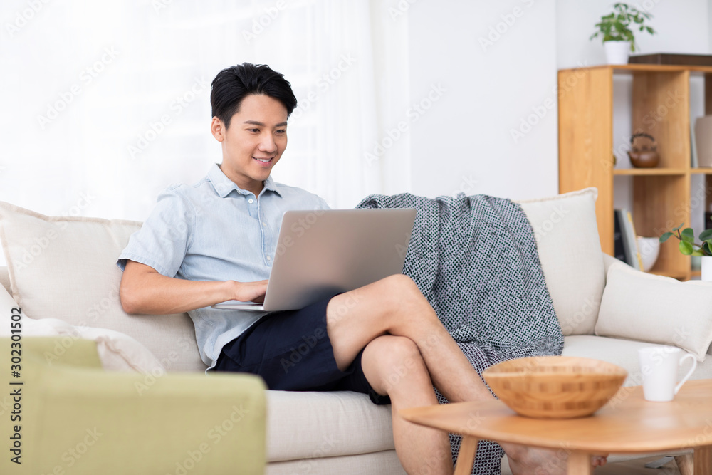 Happy young Chinese man using laptop in living room