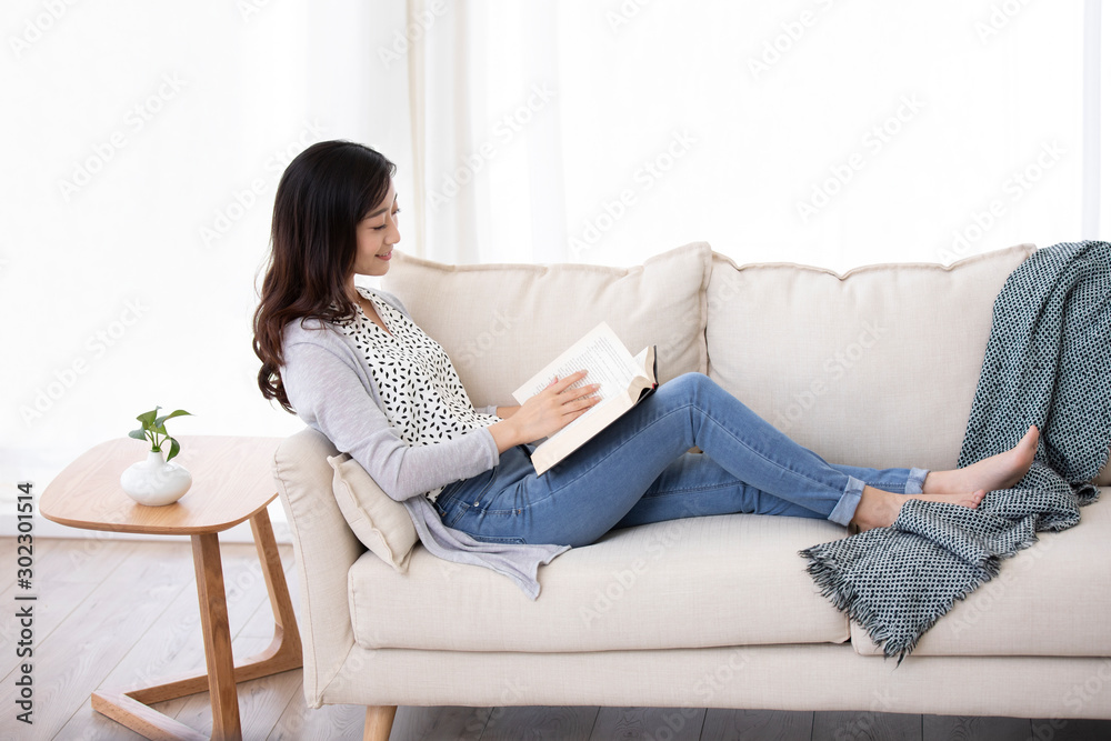Happy young Chinese woman reading book on sofa Happy young Chinese woman reading book on sofa