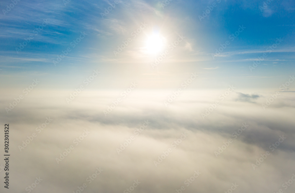 Aerial photo above the fog or white clouds with shining sun. Beautiful sunrise cloudy sky from aerial view. Above clouds from airplane window or drone.