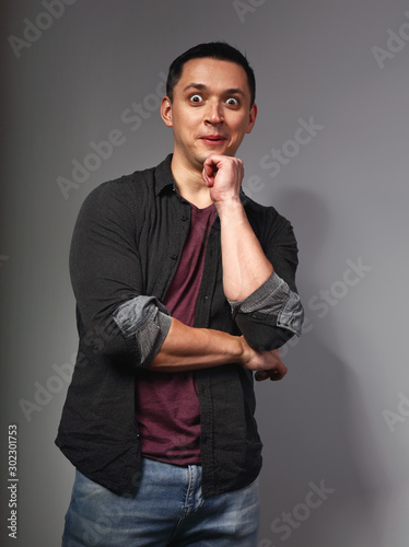 Surprising brunette man thinking and looking in purlple t-shirt with folded arms on dark grey background. Closeup photo