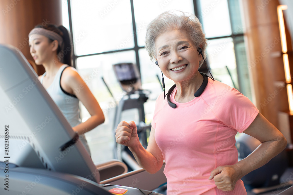 Senior Chinese woman running with wireless headphone at gym Senior Chinese woman running with wireless headphone at gym