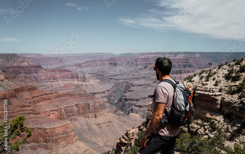 Side view of man with backpack contemplating and standing on mountain top on hot summer day in USA