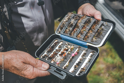 Crop aged man showing arranged lures and hooks while standing on rural street photo