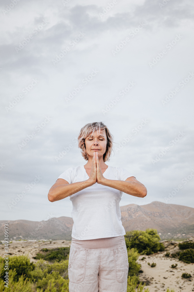 Full body barefoot adult female clasping hands over head and closing eyes while standing on rock in nature and meditating Full body barefoot adult female clasping hands over head and closing eyes while standing on rock in nature and meditating