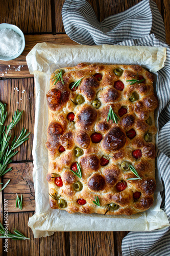 Overhead potato focaccia with fresh rosemary placed near bowl with salt and striped napkin on wooden table