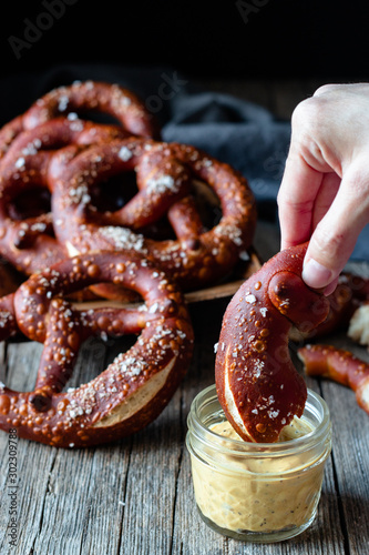 Crop person dipping homemade fresh pretzel with salt in cheese sauce on wooden table photo