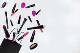 A set of cosmetics consisting of lipstick, brushes, lip gloss, eye shadow flies out of a black bag on white background. can be used in advertising and printing posters, business cards, flyers