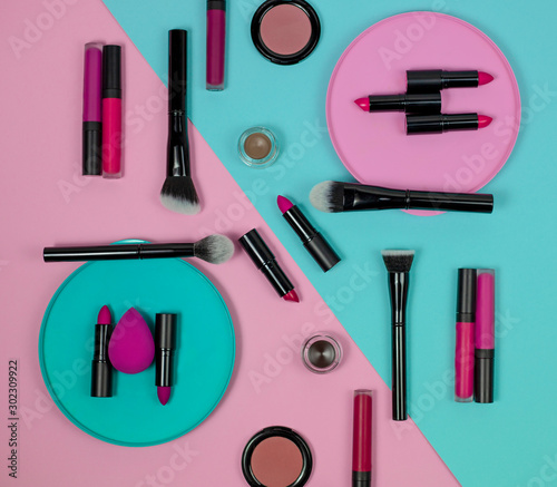 A set of cosmetics for make up, consisting of lipsticks, lip glosses, creams, foundation, blush, powder, highlighter and eye shadow lies on a pink and blue background top view. flat lay