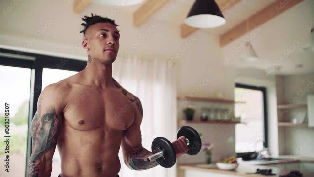 A young man doing exercise with dumbbells indoors at home, a body workout.