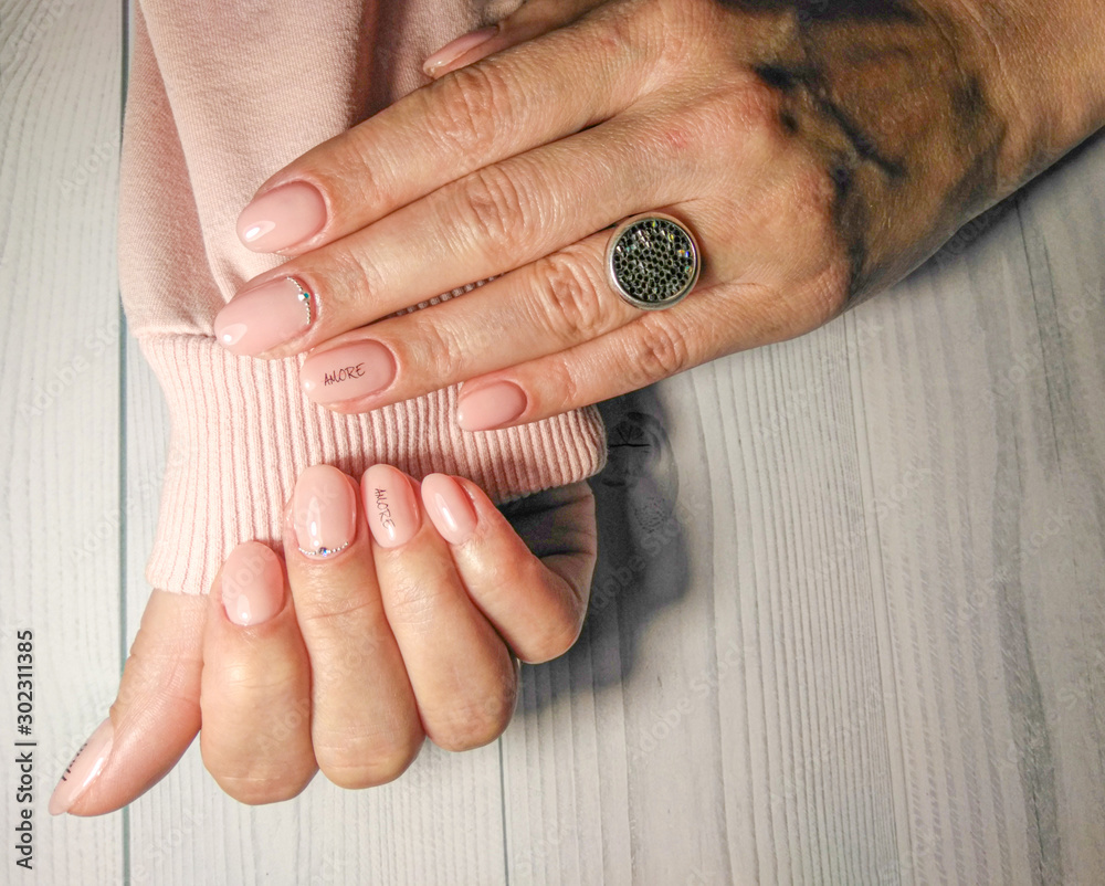 Obraz premium Delicate pink manicure on women's hands in a pink sweater. Gel lacquer pastel peach color with rhinestones design and the inscription 