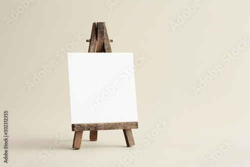 Square empty white business card template with wooden easel on bone coloured background. For branding identity, logo design pitches and marketing.