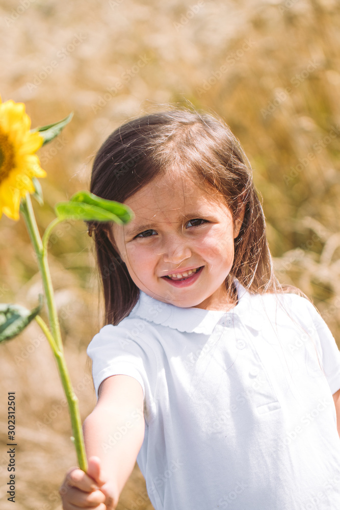 Happy little girl smelling a sunflower on the field . Happy little girl smelling a sunflower on the field .