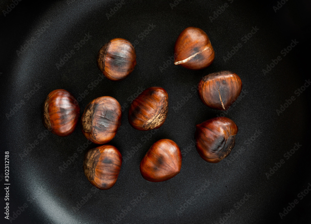 Obraz premium Chestnut on a black frying pan, top view. Roasted Chestnuts close up