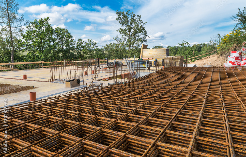 Reinforcing bars grid for ferroconcrete. Building foundations in green trees. Rebar mesh of rusty steel wires for reinforced concrete and masonry on construction site under blue sky with white clouds.