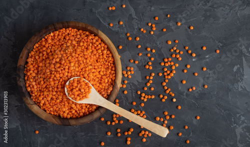 Red raw organic bio lentils in a wooden bowl with a wooden spoon stuck in it on a dark background. Place for text photo