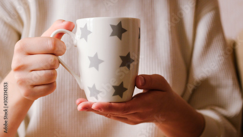 The girl in a cozy clothes drinking coffee froma a mug. hands holding hot cup of coffee or tea in morning. cup in female hands photo