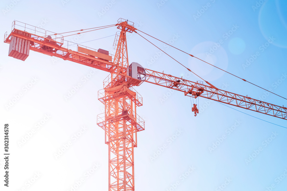 A large beautiful powerful construction crane in the rays of the rising sun against a blue clear sky at a construction site begins a working day. Modern construction equipment. Minimalism A large beautiful powerful construction crane in the rays of the rising sun against a blue clear sky at a construction site begins a working day. Modern construction equipment. Minimalism