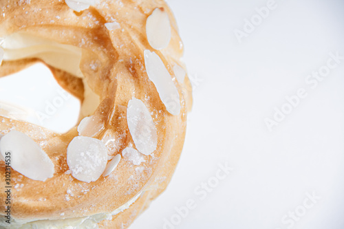 Top view of ring donut cut in the middle and inside whipped cream and on the top almond slices and sugar ppowder on white background with space for text