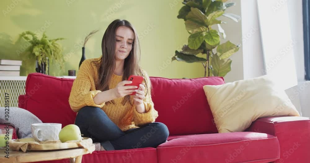 Stressful young woman sitting on sofa texting on smartphone message fighting online with boyfriend throwing mobile phone away. Breaking up. Frustration. Stressful young woman sitting on sofa texting on smartphone message fighting online with boyfriend throwing mobile phone away. Breaking up. Frustration.