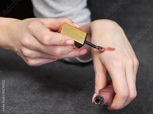 Woman's beauty blogger hands holding bottles and tubes spa professional hi-end liquid lipstick cosmetics applies sample tone color on skin with copyspace