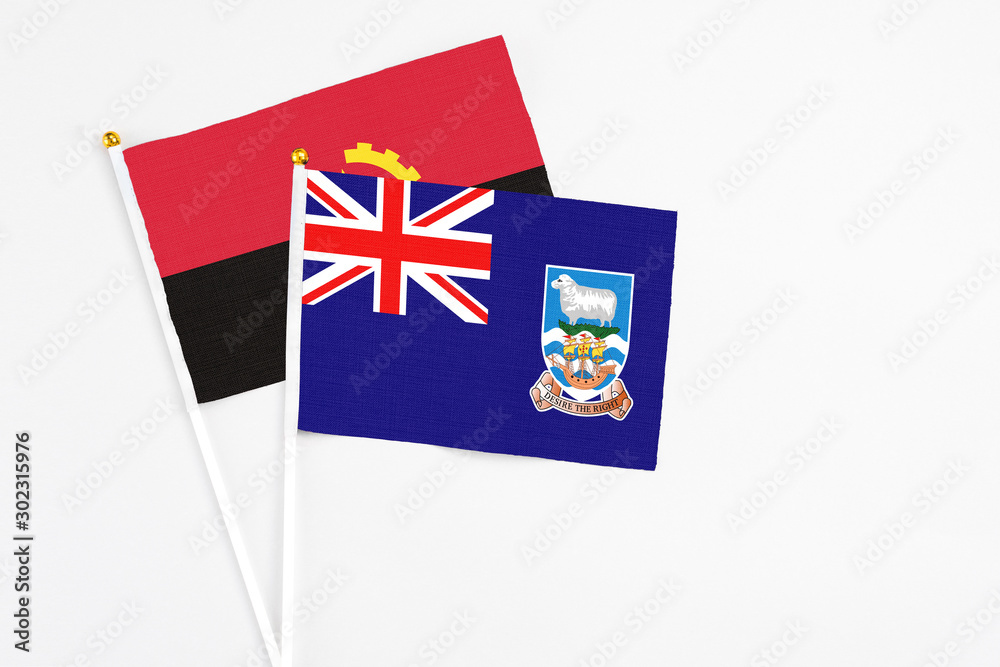 Fototapeta premium Falkland Islands and Angola stick flags on white background. High quality fabric, miniature national flag. Peaceful global concept.White floor for copy space.