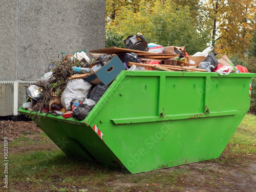 Big green color metal skip container full of tras by a house building. photo