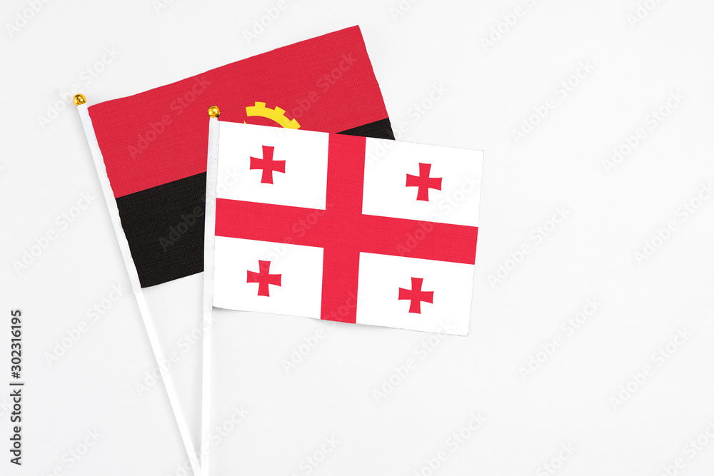 Georgia and Angola stick flags on white background. High quality fabric, miniature national flag. Peaceful global concept.White floor for copy space.